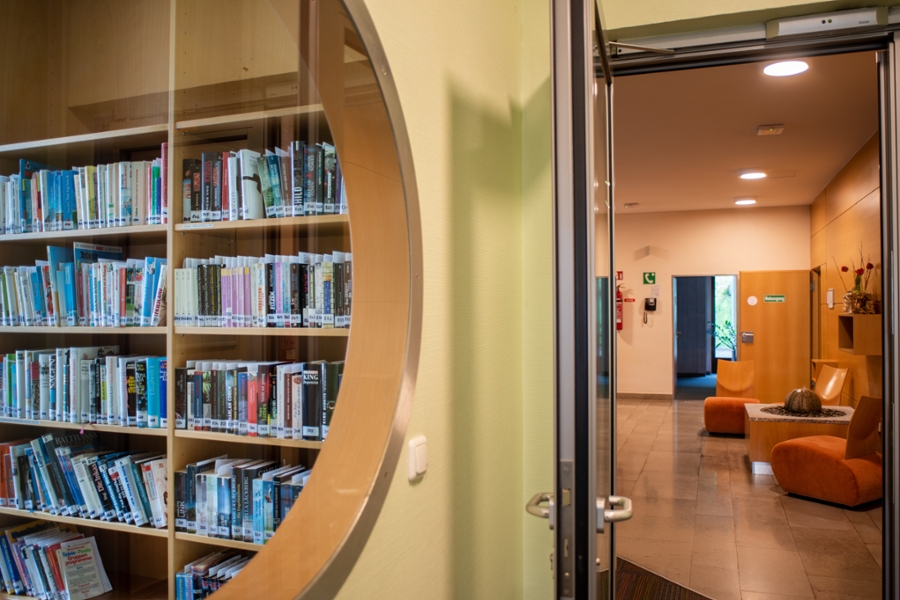 Teilweiser Einblick in die Bibliothek mit Regalen voller Bücher sowie teilweiser Einblick in das angrenzende Lesezimmer mit Sesseln.